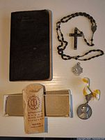 All items laid out: missal, rosary, two medals, paper sleeve, box