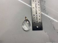 Front view of clear teardrop crystal pendant beside ruler showing length