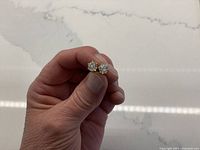 Hand holding pair of cubic zirconia stud earrings to show size and appearance