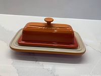 Le Creuset flame orange butter dish with lid on base, frontal view