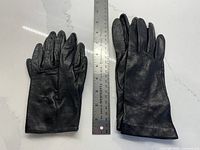 Two pairs of black leather gloves beside ruler showing length