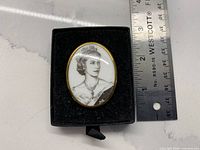 Front of brooch in display box showing portrait and gold-tone frame