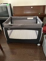 Overall view of assembled gray and black Chicco playard with mesh panels on hardwood floor