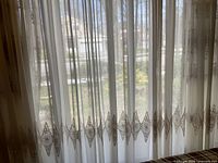 White sheer curtain panels with embroidered border and pleated header displayed hanging in daylight