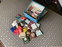 Box and loose pile of assorted matchbooks and matchboxes on tabletop