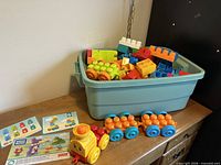 Storage bin filled with Mega Bloks, train components, instruction sheets displayed