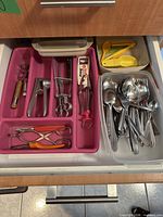Drawer with pink organiser holding metal tools and separate bin of spoons/forks