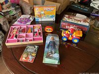 All items laid out on table including game boxes, doll, dress-up set, craft kit, ATV and dominoes