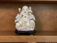Front view of multicolor porcelain Laughing Buddha figurine on wood stand