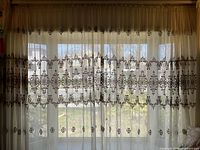 Full view of sheer panels hanging over window showing embroidery pattern