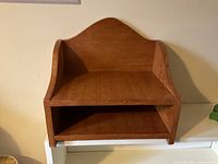 Front view of small stained wood tabletop shelf showing two open tiers and arched back