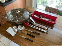 Overall lot showing steamer pot with lid, insert, utensil assortment, red tray
