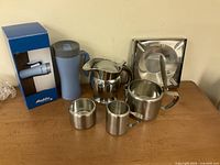 Group shot of all stainless pieces, travel mug and box