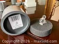 Clear crystal duck figurine on gray foam lid with cylindrical storage tube shown