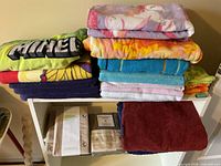 Stacks of assorted themed and solid towels with packaged liners and pillowcases on shelf