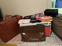Overview of brown briefcase, portfolio, assorted pouches on box, partial view of rolling suitcase
