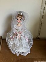 Front view of bride doll in lace gown and veil on stand