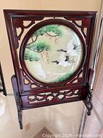 Front view of entire screen on stand showing rotating circular embroidered panel with cranes