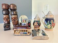 Group shot showing all eight items: two beer steins, tiki pair, cable car, snow globe, hip flask, guard in sentry box
