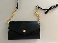 Front view of black clutch purse showing envelope flap, gold-tone button clasp and chain strap