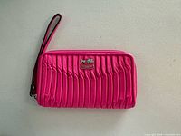 Front view of pink pleated Coach wristlet wallet showing logo plaque and wrist strap