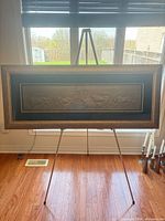 Overall view of framed metal relief plaque on easel