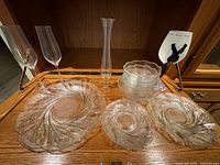 All glass items arranged on wooden shelf surface: platter, plates, bowls, vase, flutes, plaque