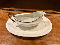 Side view of the porcelain gravy boat resting on its underplate, showing gold-tone handle and rim detail