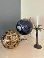 Globe, gold orb, and palm candlestick grouped on surface