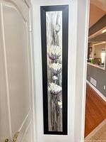 Full view of the tall, narrow framed floral artwork hanging on wall