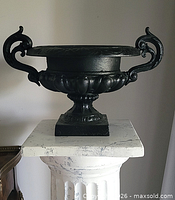 Front view of black cast metal urn planter on pedestal