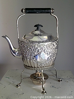 Front view of silver-plated tilting kettle on stand with burner