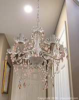 Full view of chandelier hanging with six arms, pink crystal drops and chain