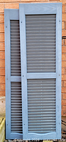 Two blue-grey louvered shutters leaning against wall