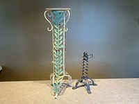 Tall painted pedestal candle stand beside small dark spiral holder