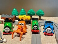 Front view of four character engines, orange vehicle, tanker, passenger coach, trees on grey track