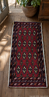 Full view of red Turkmen mat on wooden floor