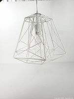 Overall view of white geometric cage pendant light suspended, showing wireframe shade