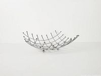 Side view of chrome grid fruit bowl showing curvature and ball feet