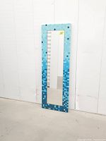 Front view of full-length blue ombre mosaic mirror leaning against wall