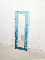 Full view of rectangular mirror leaning against wall showing complete mosaic frame