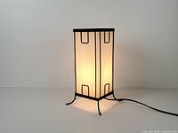 Lamp illuminated, front angled view shows frame, shade, cord, feet