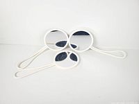 Three white round Umbra shower mirrors laid flat, showing front surfaces and loop handles