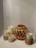 Group shot of three rattan-wrapped candles, glass vase with sleeve, and spherical rattan lantern