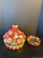 Apple motif covered dish next to stack of five decorative glass plates