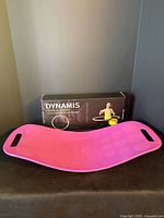 Pink balance board in front of boxed Dynamis hula hoop