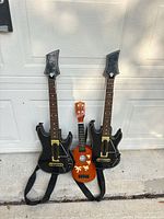 Three instruments standing against garage door: two black Guitar Hero controllers and one brown ukulele