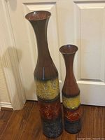 Two tall metal vases side by side showing color bands and relative size