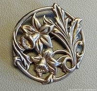 Front view of round sterling silver brooch with daffodil design