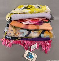 Stack of seven assorted scarves showing colors, patterns and fringe